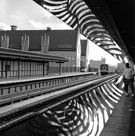 B&W man waiting on elevated train station