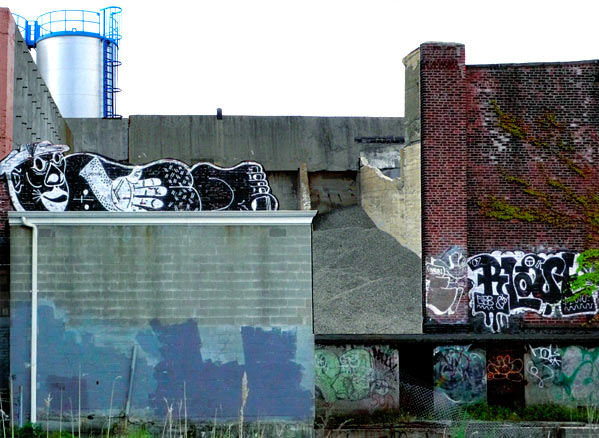 Graffiti surrounding a shed, reclining man in black and white on the roof