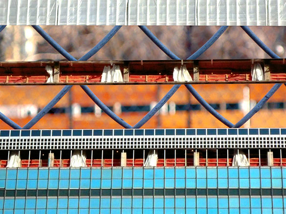 Turquoise grid of windows broken a close-up of the diamond pattern of a chain-link fence.