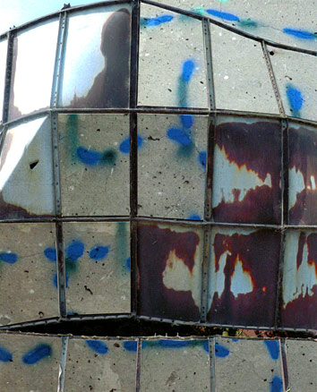Rusty patches of old silo structure interspersed with cracked concrete, cracks spray-painted blue.