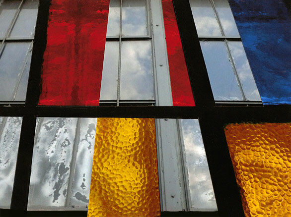 Looking up at factory windows collaged together with stained glass window of checkered colors.